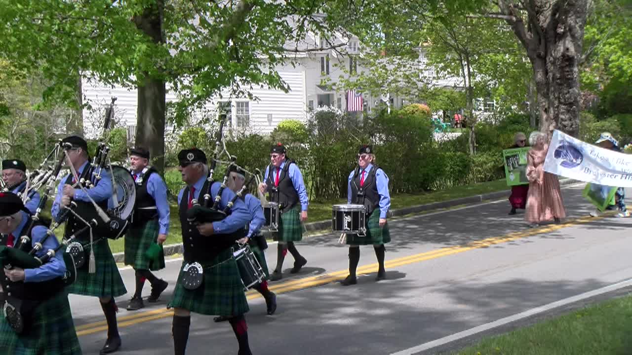 Eight people in a bagpipe band walking down the middle of a two lane road on a spring day