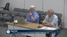 Thumbnail of meeting video shows two people sitting at the presenters tables in meeting room a.