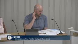 The health director is sitting behind a table at the board of health meeting
